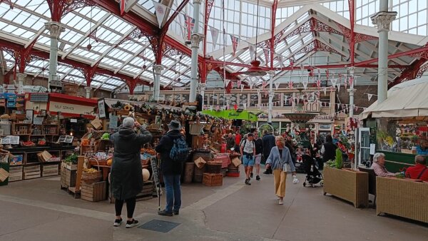 Innenaufnahme mit Marktständen und vorbeigehenden Personen des Central Markets in St. Hélier, Jersey. 