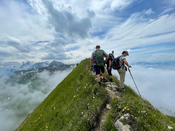 Drei Personen drängen sich auf schmalem Gratweg mit Abgrund rechts und links