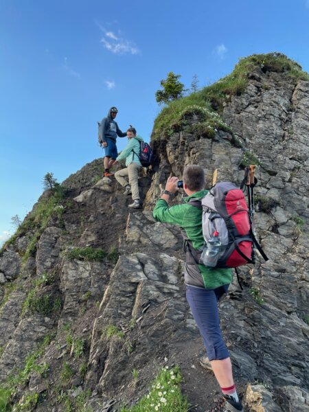 3 Wanderer klettern einen Felsvorsprung hinauf.