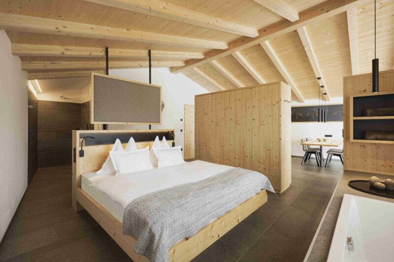 Ein grosses Bett steht in einem Schlafzimmer aus hellem Holz. 
