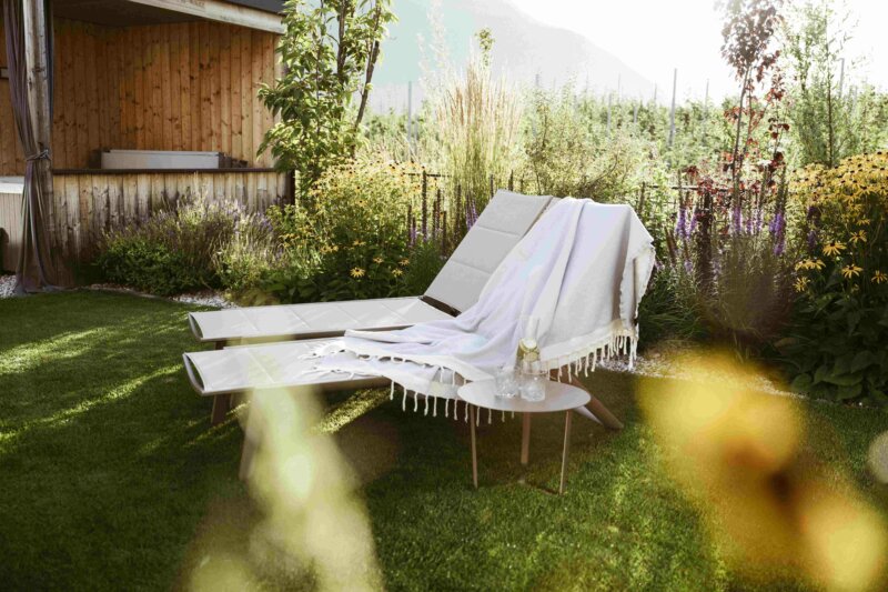 Zwei weisse Liegestühle stehen in einem sonnigen, grünen Garten.