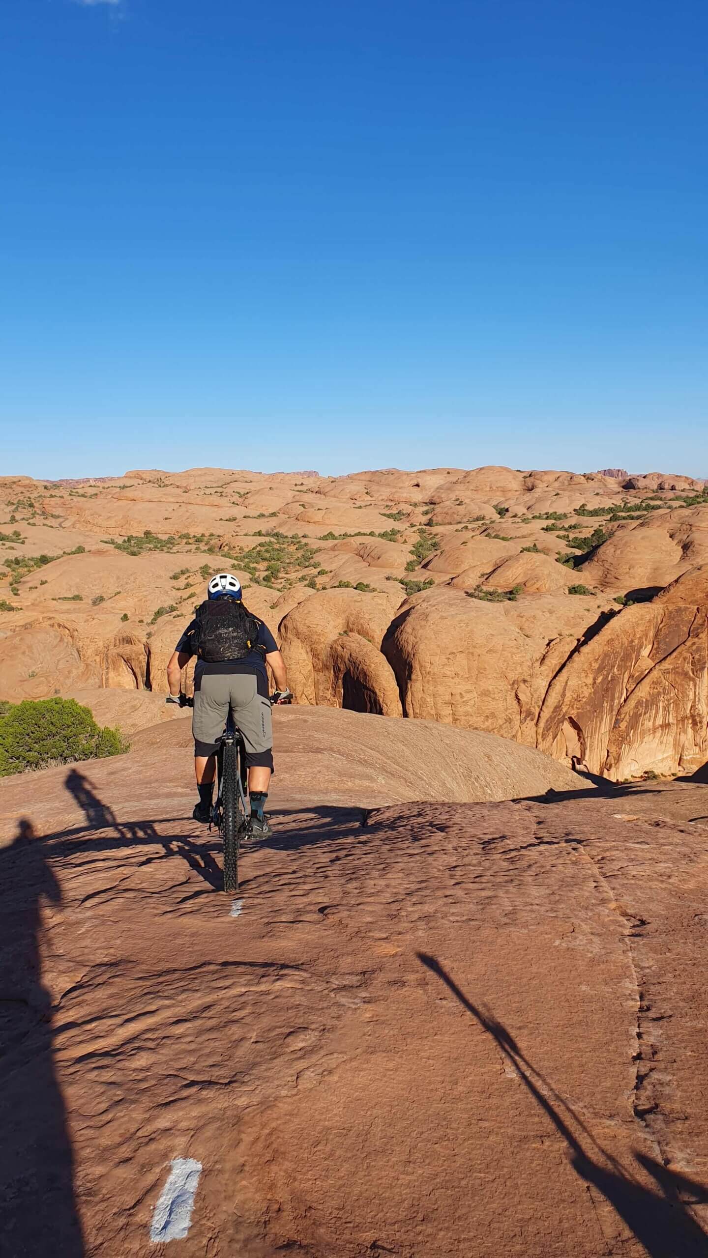 Ein Mountainbiker folgt einer weissen Markierung in einer roten Sandsteinlandschaft.