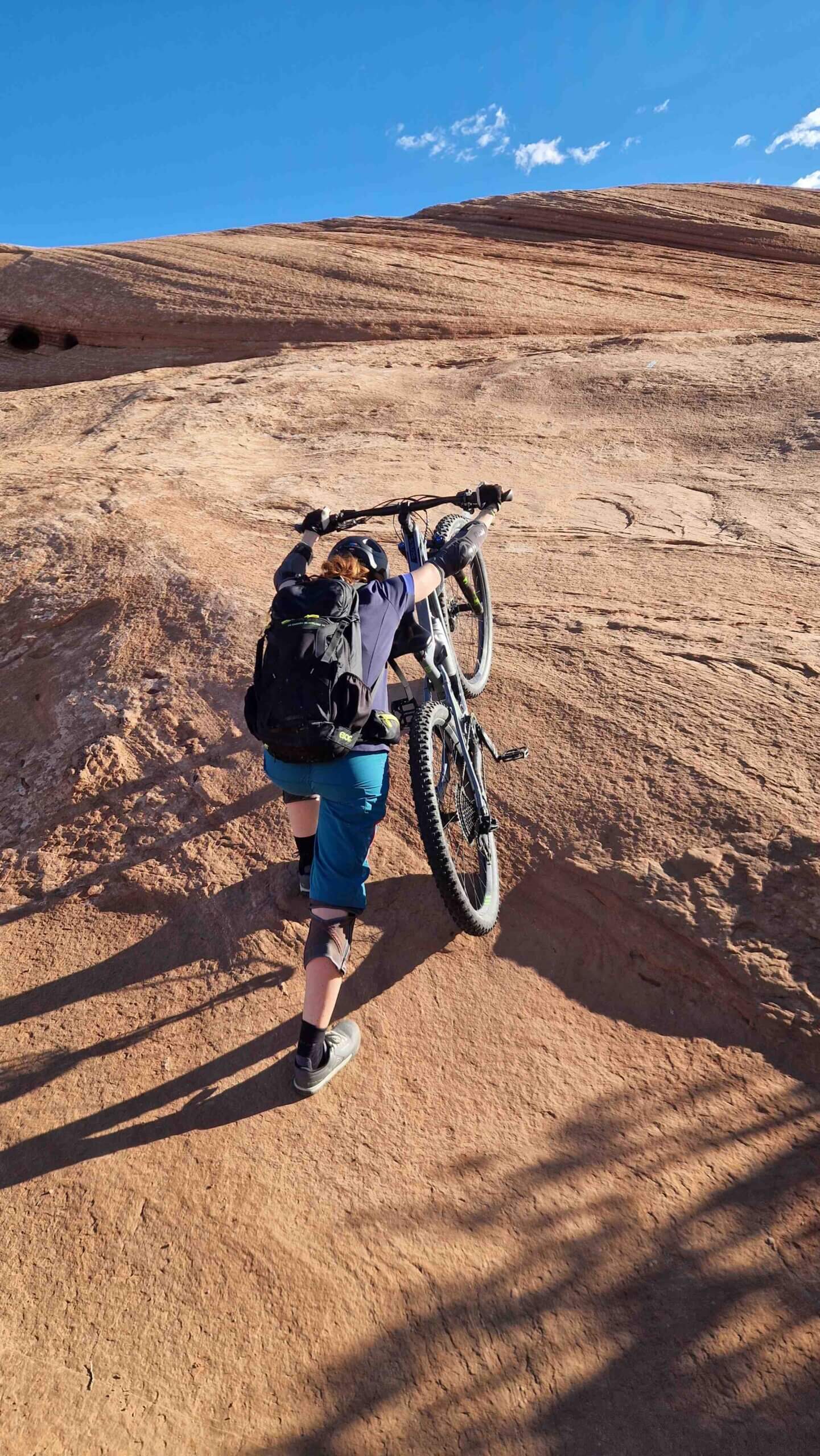 Mountainbikerin stösst ihr Mountainbike einen steilen Anstieg hinauf.