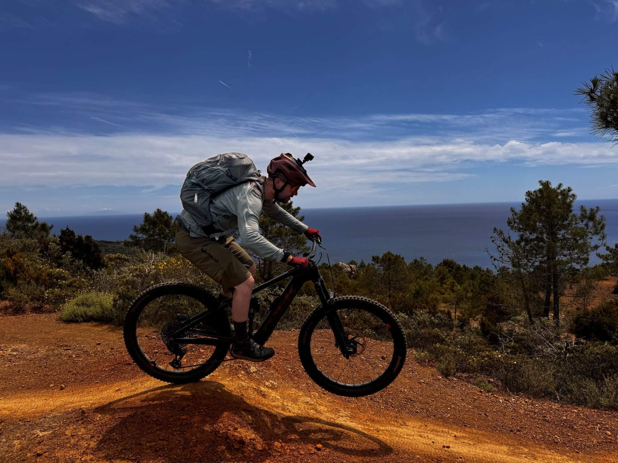 Mountainbiker auf Elba fährt auf roter Erde, dahinter blaues Meer