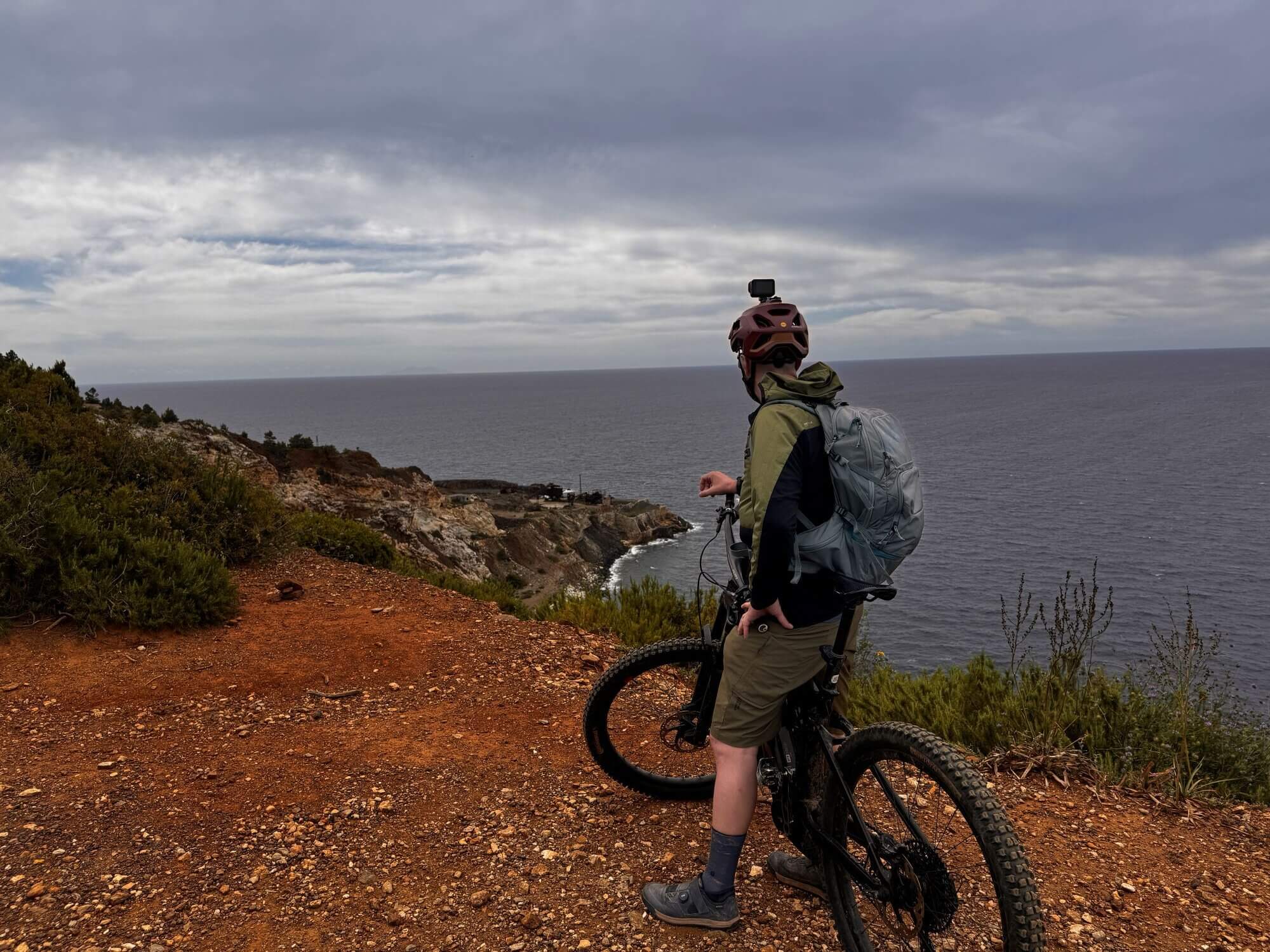 Mountainbiker auf Elba steht auf roter Erde und blikt auf blaues Meer