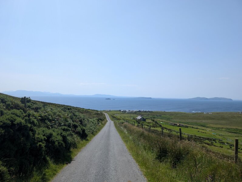 Strasse, links und rechts Wiese, dahinter Meer