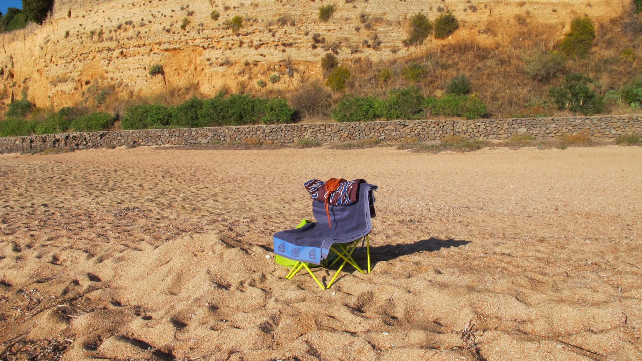 Campingstuhl mit Handtuch und Bikini auf dem Sanststrand Cala Gonone in Sardinien.
