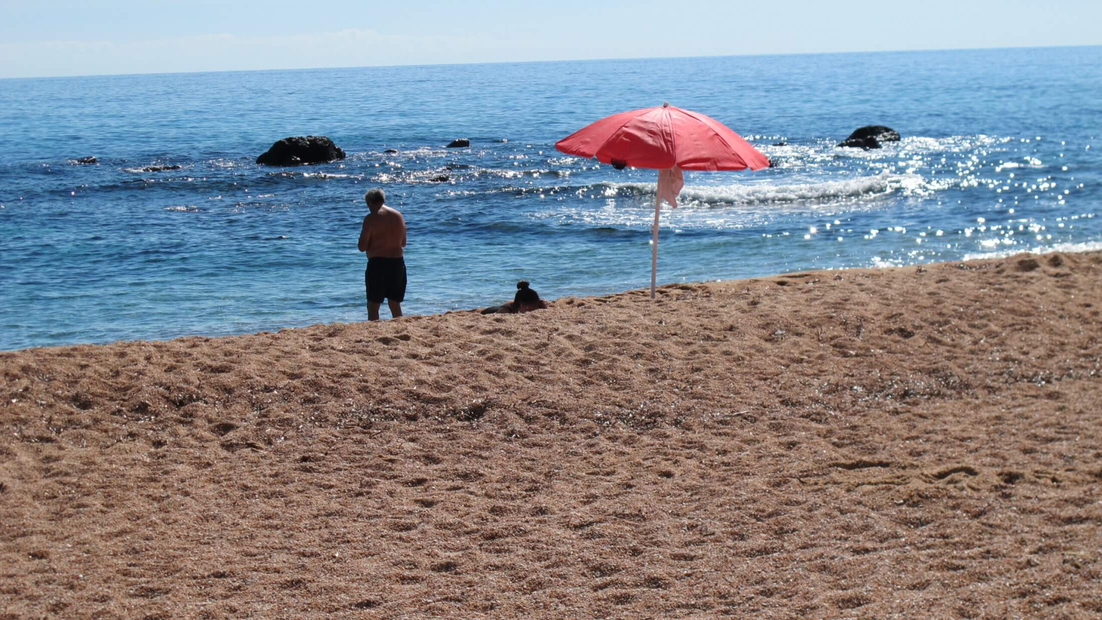roter Sonnenschirm und Mann auf dem Sandstrand Cala Gonone