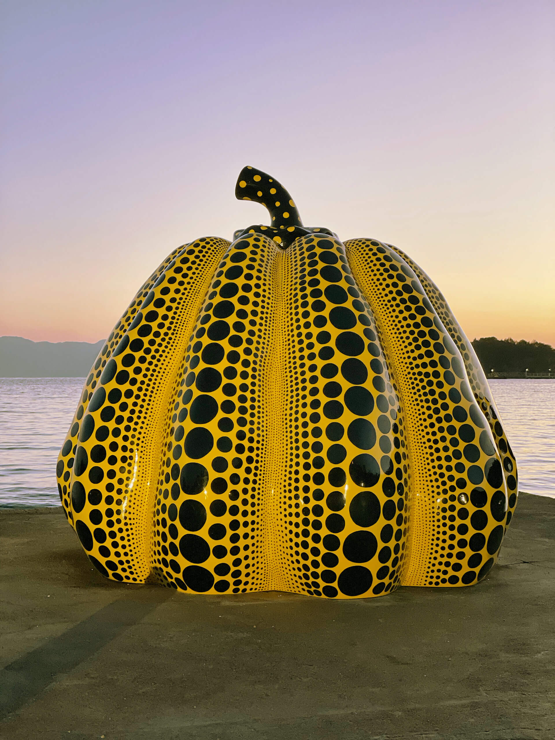 Skulptur von einem gelben Kürbis mit schwarzen Punkten vor dem Sonnenuntergang in Naoshima