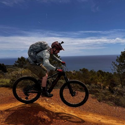 Mountainbiker auf Elba fährt auf roter Erde, dahinter blaues Meer
